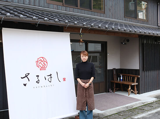 [写真]店舗前にて，店主の谷央子さん。