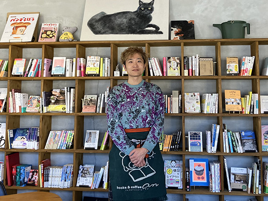 [写真]壁一面に並ぶ蔵書の前で、店主の佐藤さん。