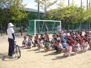 運動場で子どもが座って自転車の乗り方の話を聞いている写真